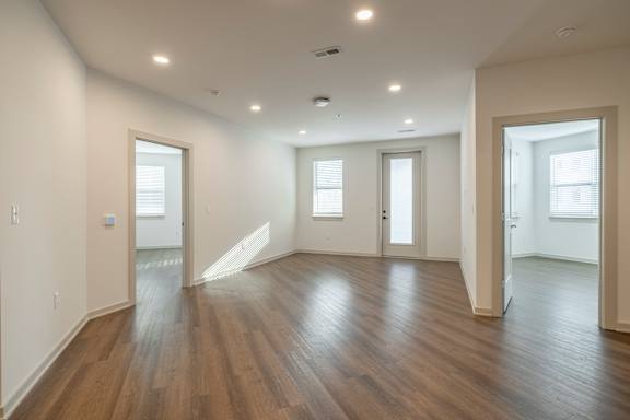 A spacious room with wooden floors and three windows.