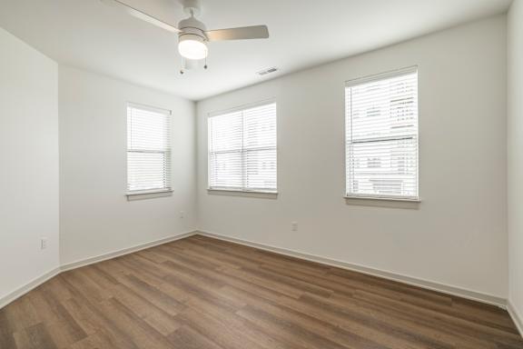 A room with a ceiling fan and two windows.