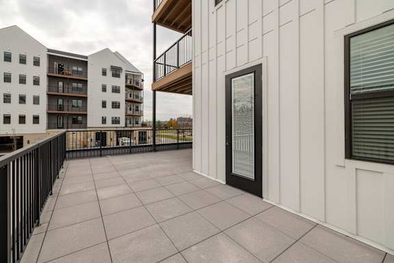 A balcony with a black railing and a white building in the background.