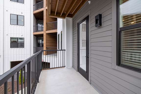 A balcony with a black railing and a grey wall.