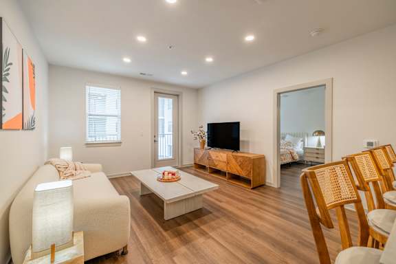 A living room with a white sofa, wooden chairs, and a television.