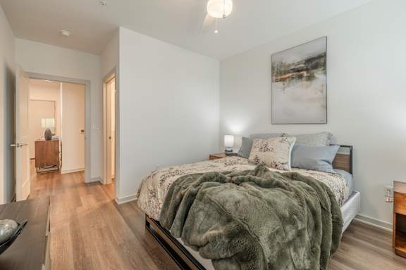 A bedroom with a bed covered in a grey blanket and a painting hanging on the wall.