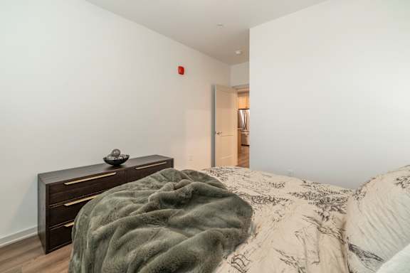 A bedroom with a bed, a dresser, and a doorway leading to another room.