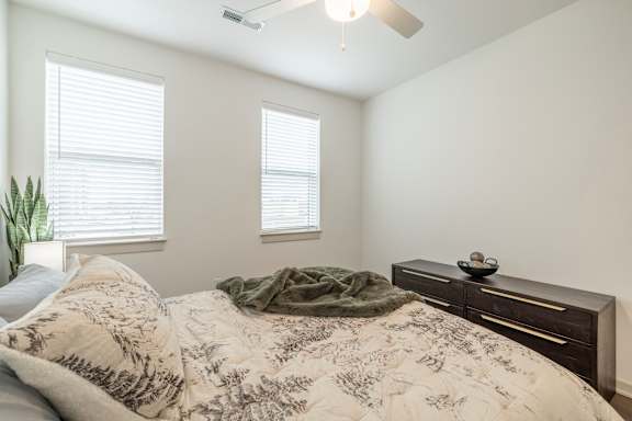 A bedroom with a bed, a plant, and a ceiling fan.