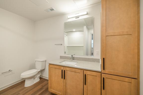A bathroom with a toilet, sink, and wooden cabinets.