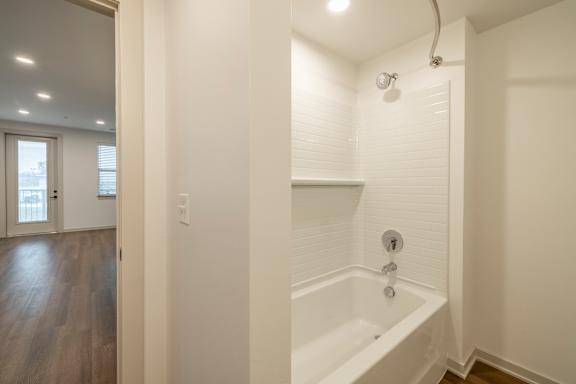 A white bathroom with a tub and a doorway leading to another room.