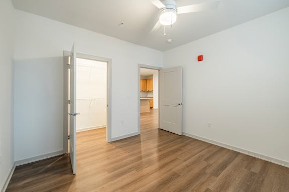 A room with a wooden floor and white walls with a door open to another room.