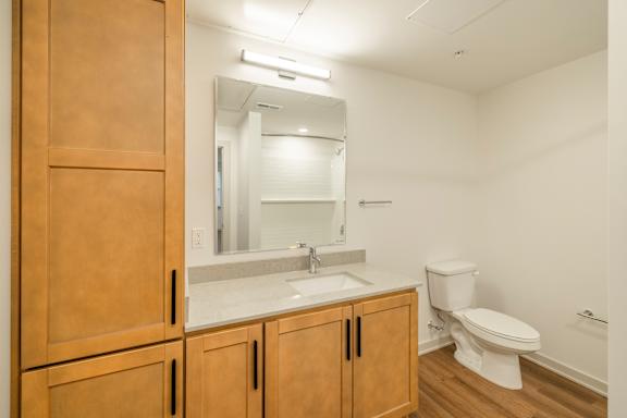 A bathroom with a toilet, sink, and wooden cabinets.