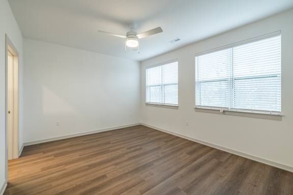 A room with wooden floors and two windows with blinds.