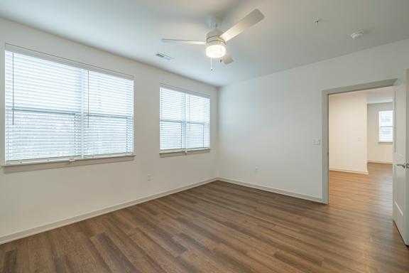 A room with wooden floors and two windows with blinds.
