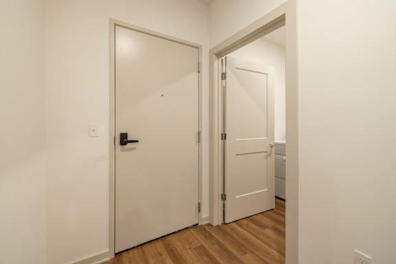 A white door with a black handle is open to a hallway.