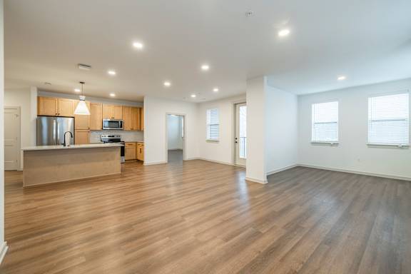 A spacious room with wooden floors and a kitchen area with a refrigerator, microwave, and oven.