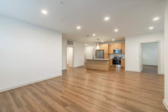 A spacious room with wooden flooring and a kitchen area in the background.