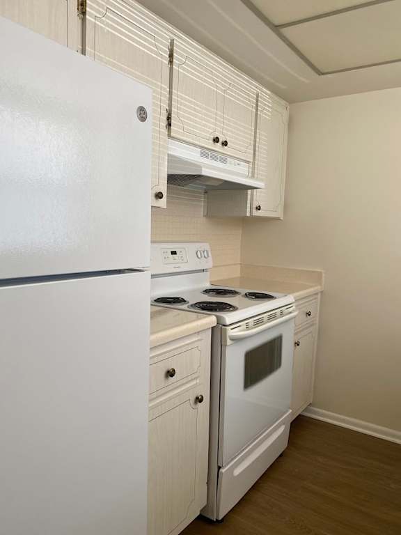 A white refrigerator is in a kitchen with a stove and cabinets.