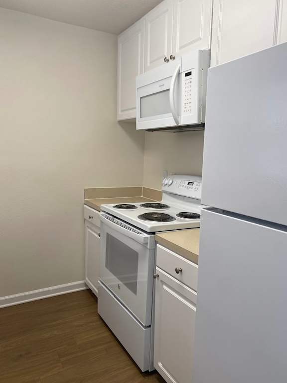 A white kitchen with a stove, oven, microwave, and refrigerator.