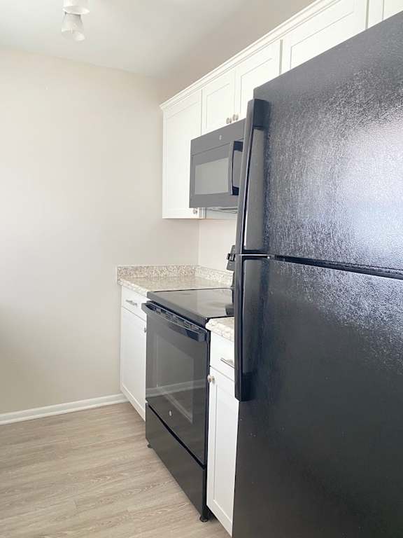 A black refrigerator in a kitchen with white cabinets.