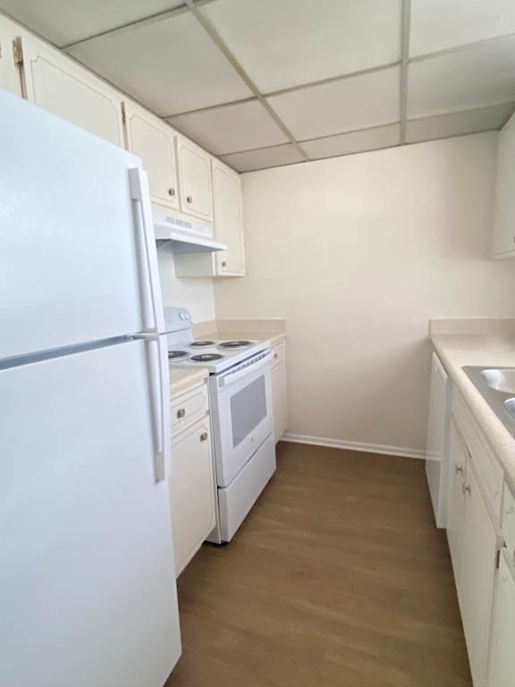 A white refrigerator is in a kitchen with white cabinets and a white stove.