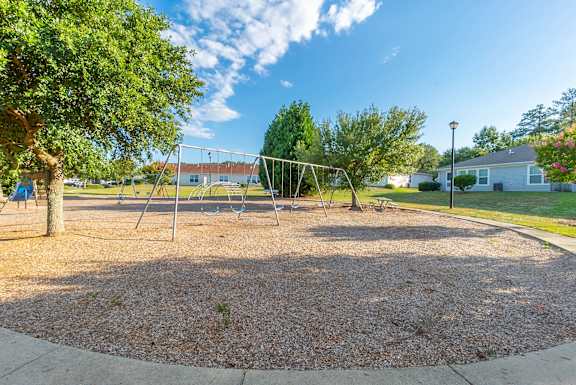 a swing set in a playground in a park with trees  at Huntington Village **, Warner Robins, GA, 31098