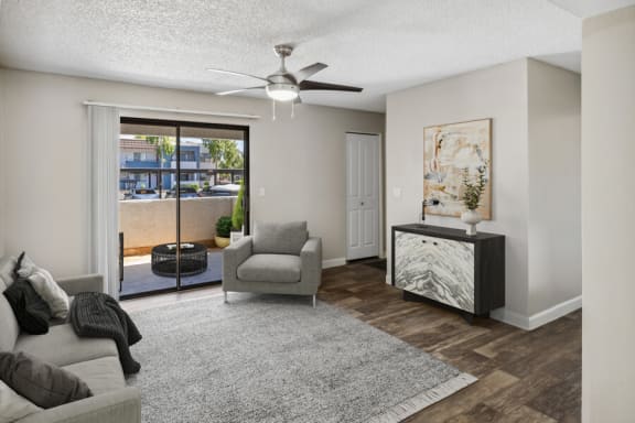 Chandler, AZ, Apartments - Chandler Ridge - A Living Room Features A Sofa And Armchair On A Large Rug, Wood-Style Flooring, Ceiling Fan, And Console Cabinet With Wall Art.