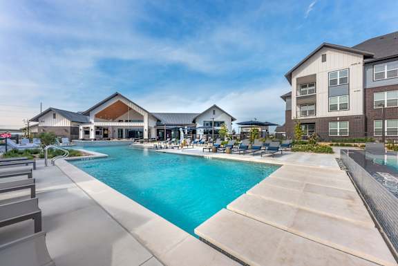A large swimming pool is surrounded by a concrete patio and lounge chairs.