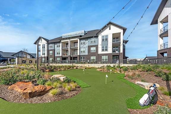 A golf hole is in the front yard of a large apartment complex.