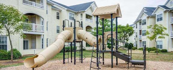 A playground with a slide and a climbing frame in front of apartment buildings.