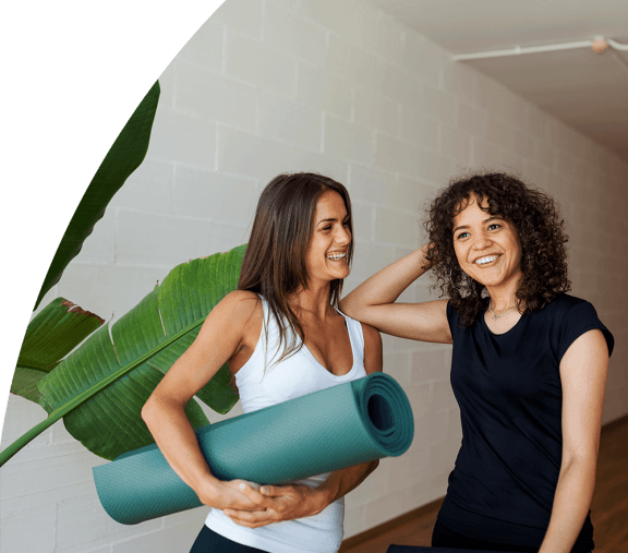 two women standing next to each other holding a yoga mat