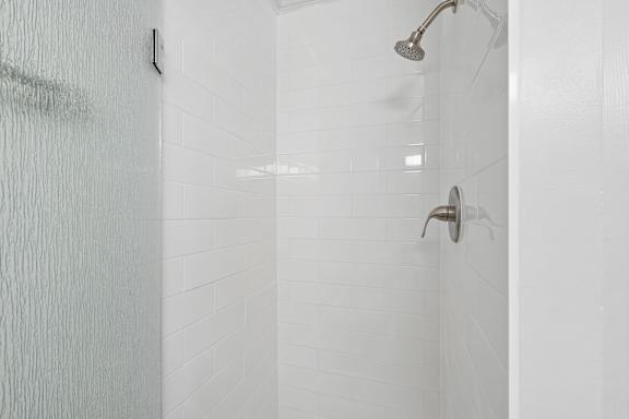 A white tiled shower with a shower head and hand held shower.