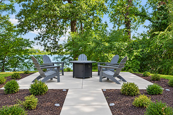 A concrete patio with a table and chairs surrounded by greenery.