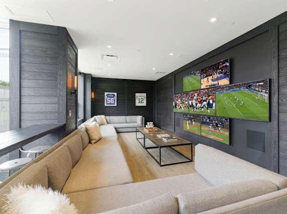 A modern living room with a large couch and a TV displaying a soccer game.