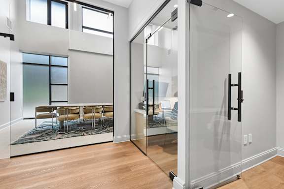 A glass door separates a room with a table and chairs from another room.