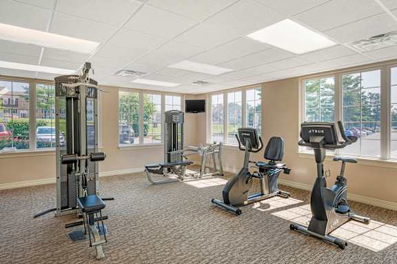A gym with a variety of equipment including a treadmill, elliptical machines, and a weight machine. at The Apartments at Hunters Glen, Frederick, MD