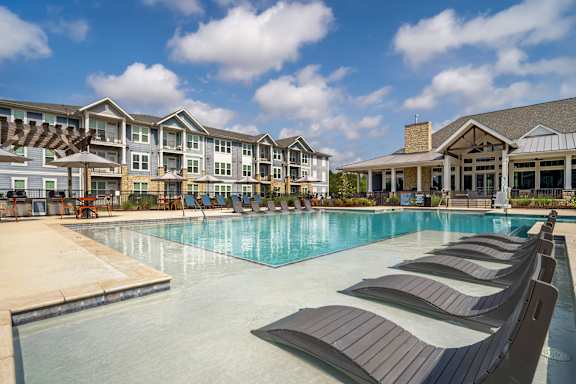 A large swimming pool with lounge chairs in front of a resort-style building.