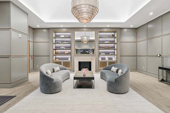 A modern living room with grey and white decor, a fireplace, and a chandelier.