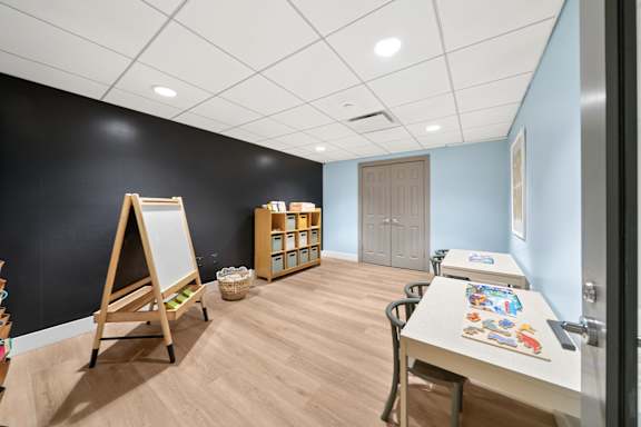 A room with a whiteboard, a table with art supplies, and a cabinet with shelves.