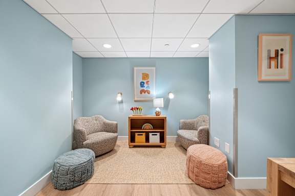 A room with blue walls and a wooden floor with a chair, ottoman, and table.