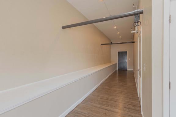 A long hallway with a white wall and a wooden floor.
