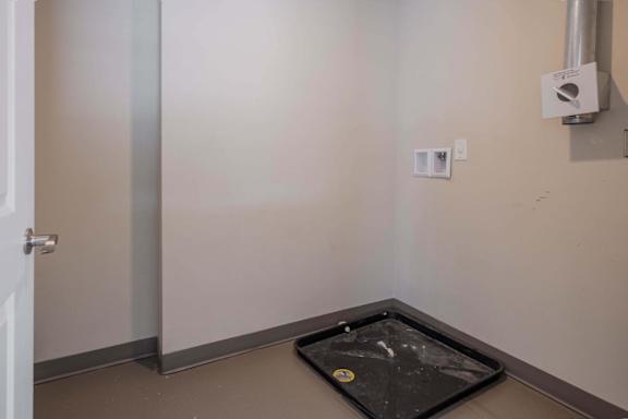 A room with a door, a wall-mounted speaker, and a black tray on the floor.