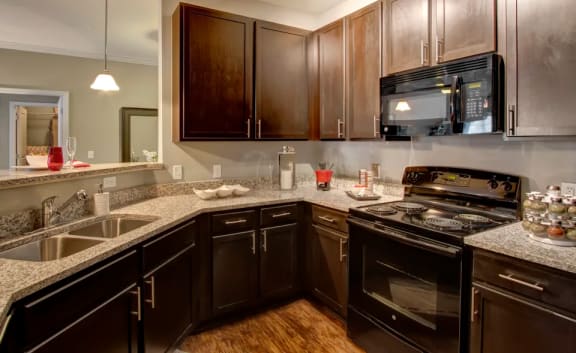 Kitchen, granite countertops, wood-like flooring, black appliances, dark wooden cabinets, at Enclave at Bailes Ridge Apartment Homes, Indian Land, SC