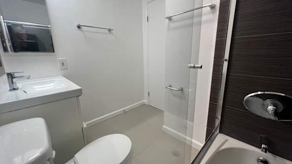 A white toilet is in a small bathroom with a sink and a shower.
