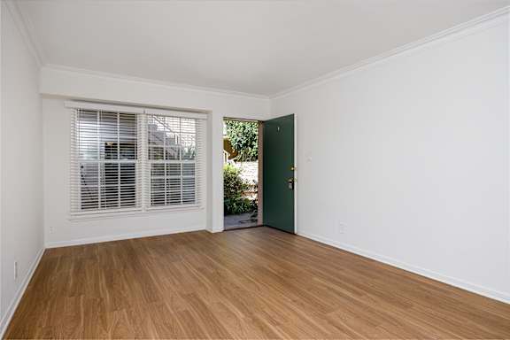 a living room with white walls and wood floors and a green door
