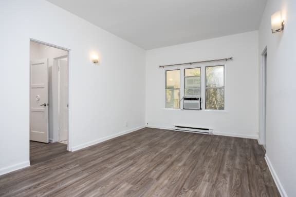 a living room with white walls and wood floors and a window