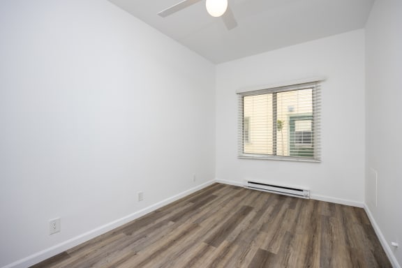 an empty room with white walls and wood floors and a window