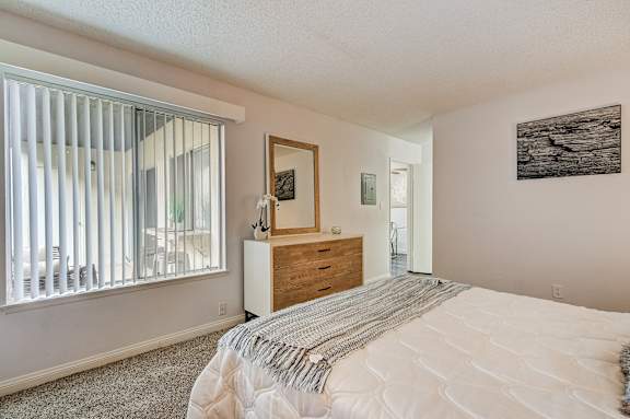 the master bedroom has a large window with blinds and a bed and dresser