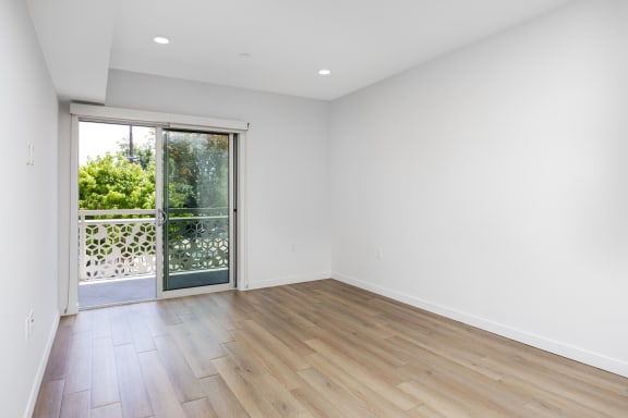 an empty living room with a sliding glass door to a balcony