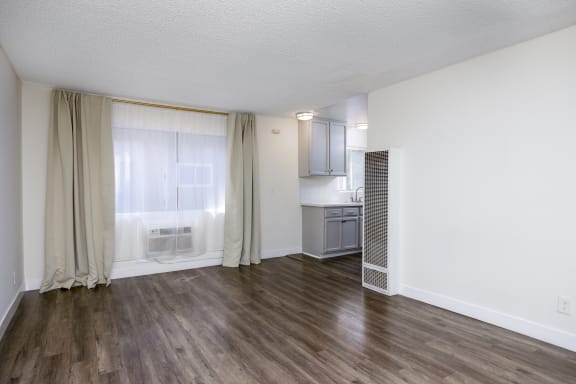 the living room and kitchen of an apartment with wood flooring and a large window