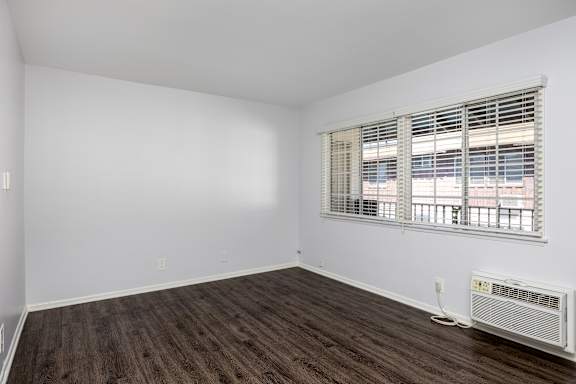 an empty room with white walls and wood flooring and a window