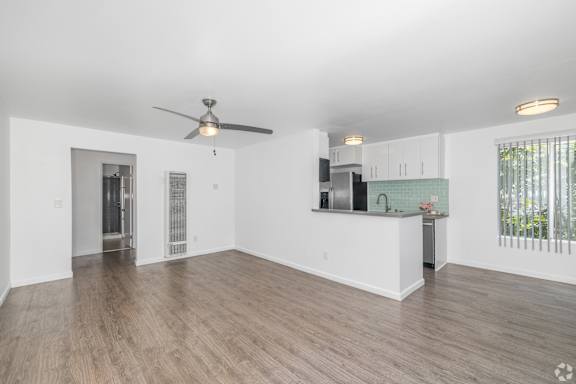 A spacious living room with a ceiling fan and hardwood flooring.
