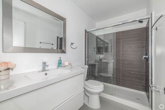 A white bathroom with a toilet, sink, mirror, and shower.