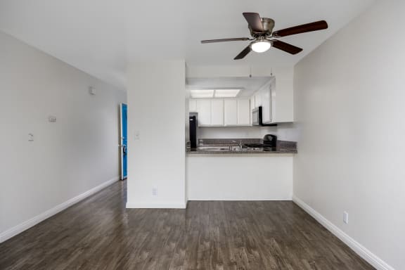 an empty living room with a ceiling fan and a kitchen